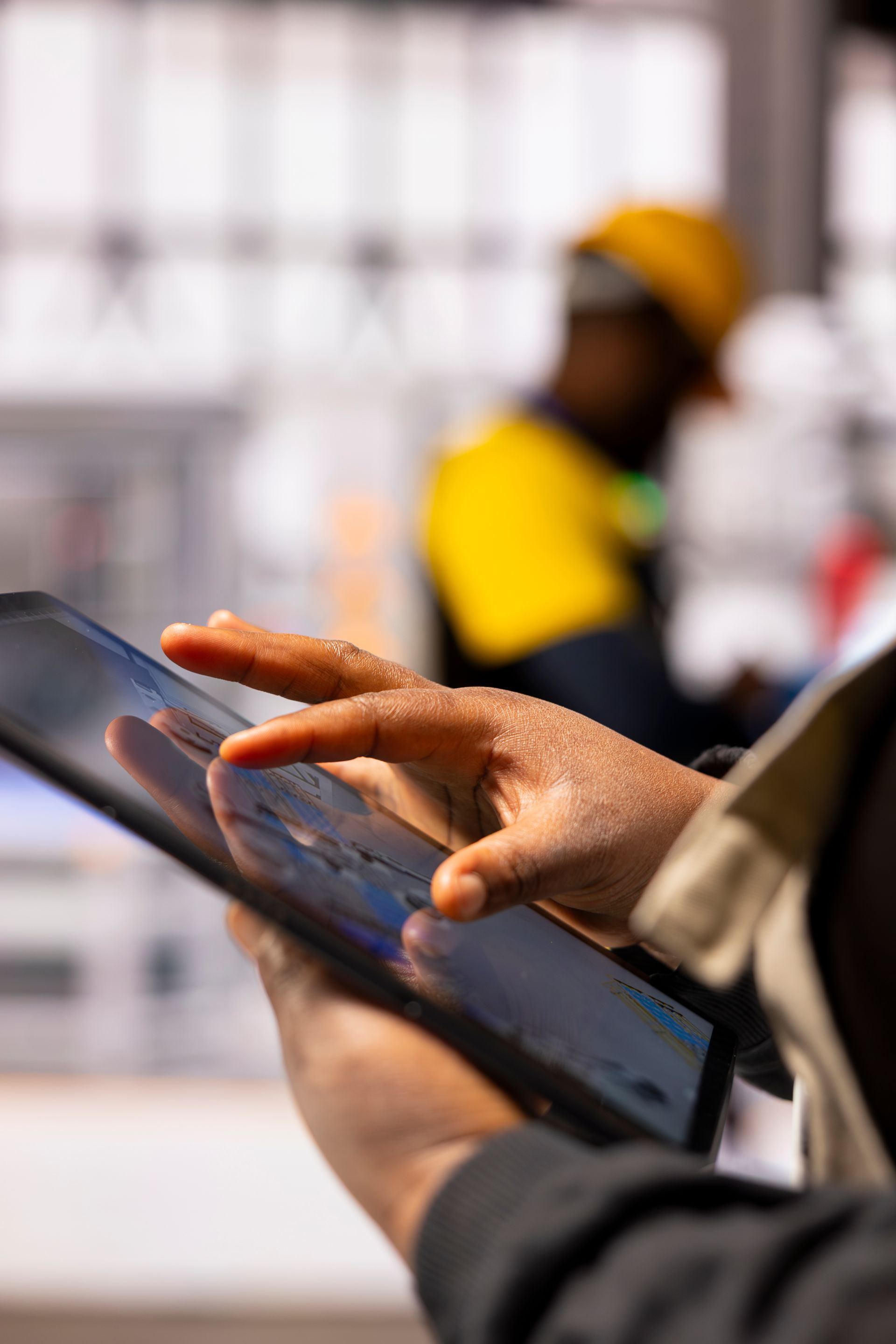 Evaluating the ability to influence loss outcomes and financial return. A close-up of hands using a digital tablet to review site data on a construction project, with a blurred worker in a high-visibility yellow vest in the background, illustrating a hands-on, operator-focused assessment.
