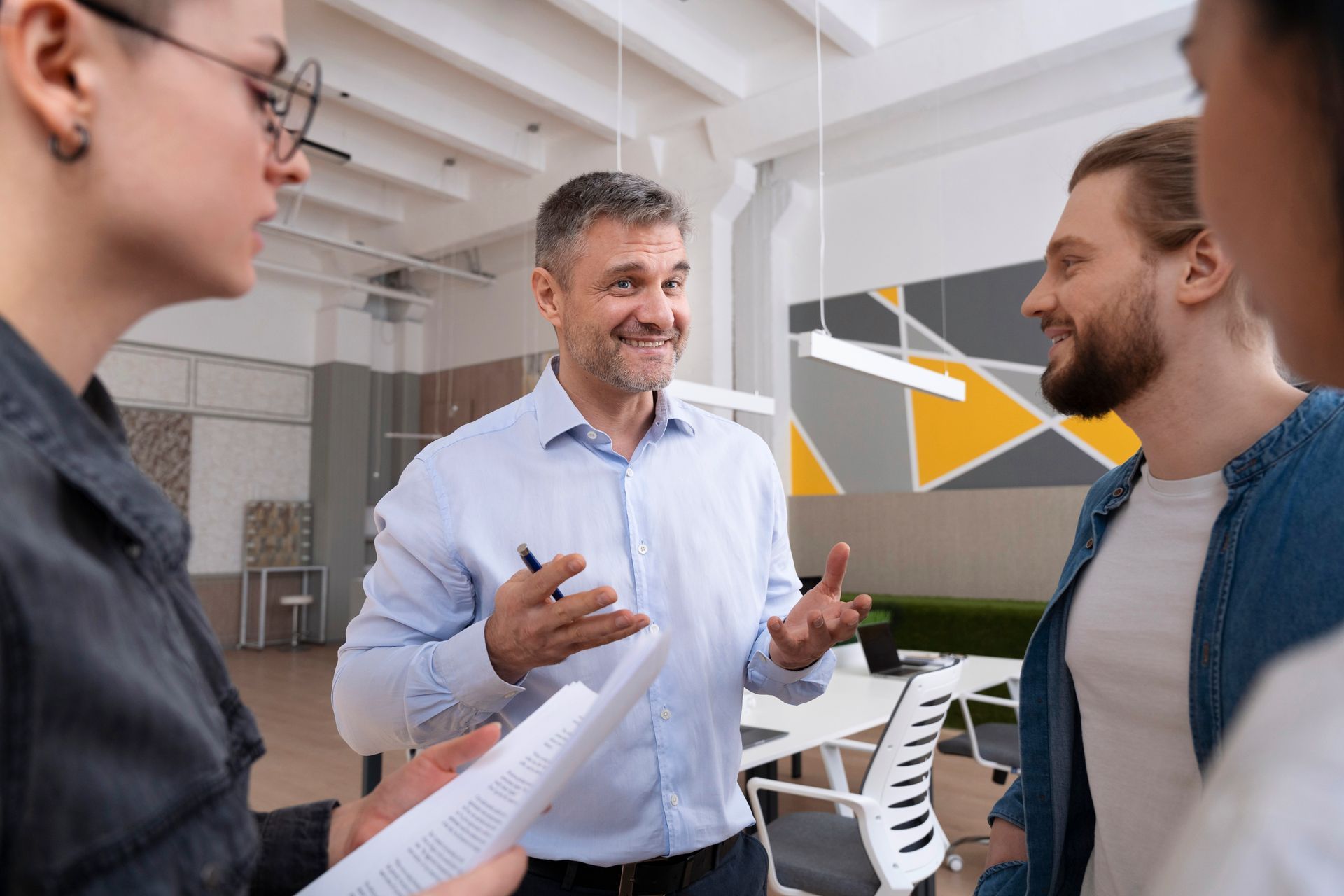 Tracking financial KPIs to drive increased premium returns. A smiling, confident business leader in a light blue shirt gesturing during a positive discussion with colleagues, representing the successful achievement of financial KPIs and premium returns within a group captive.