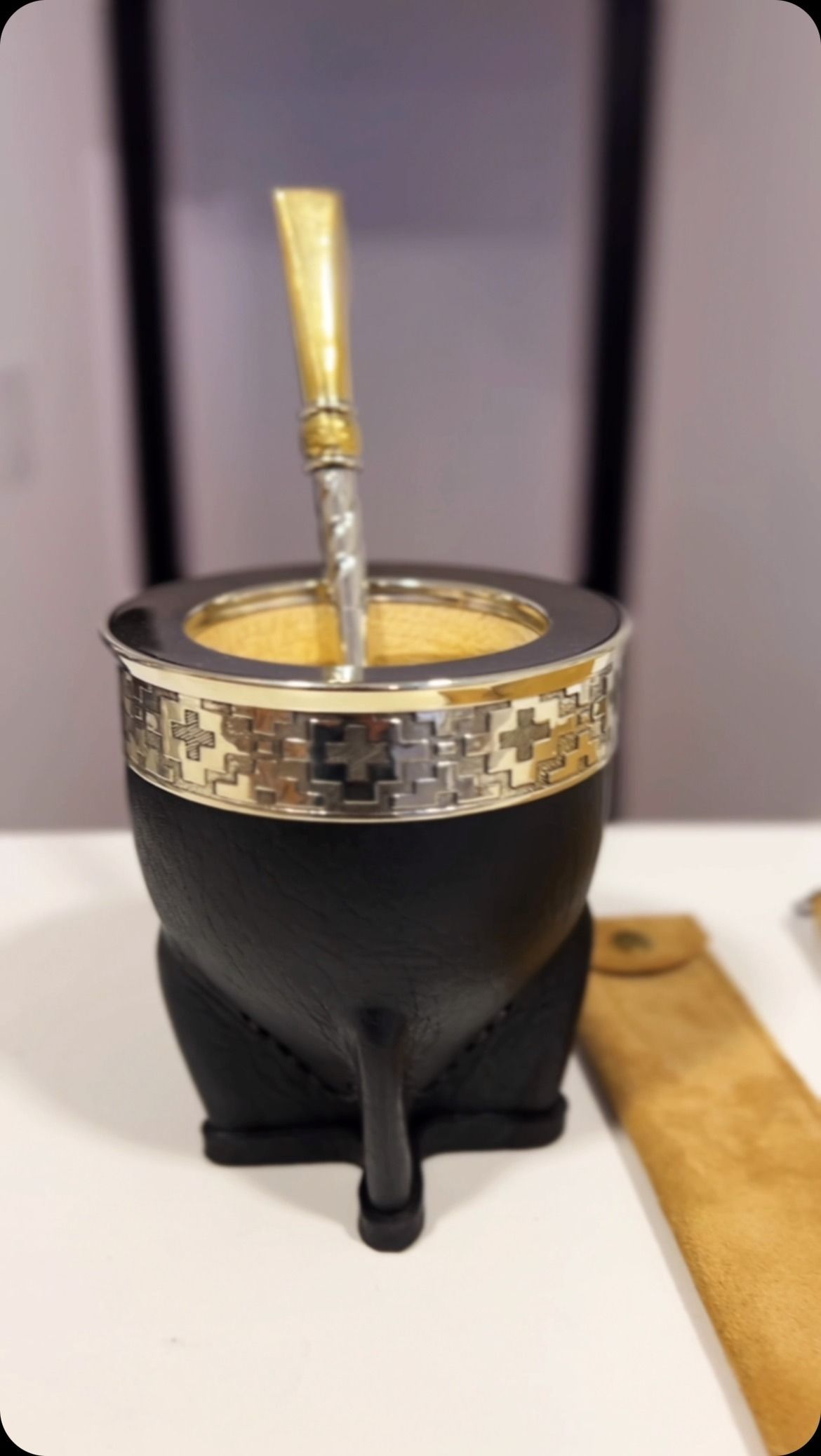 Mate negro con borde plateado, pajita y estuche de cuero sobre superficie blanca.