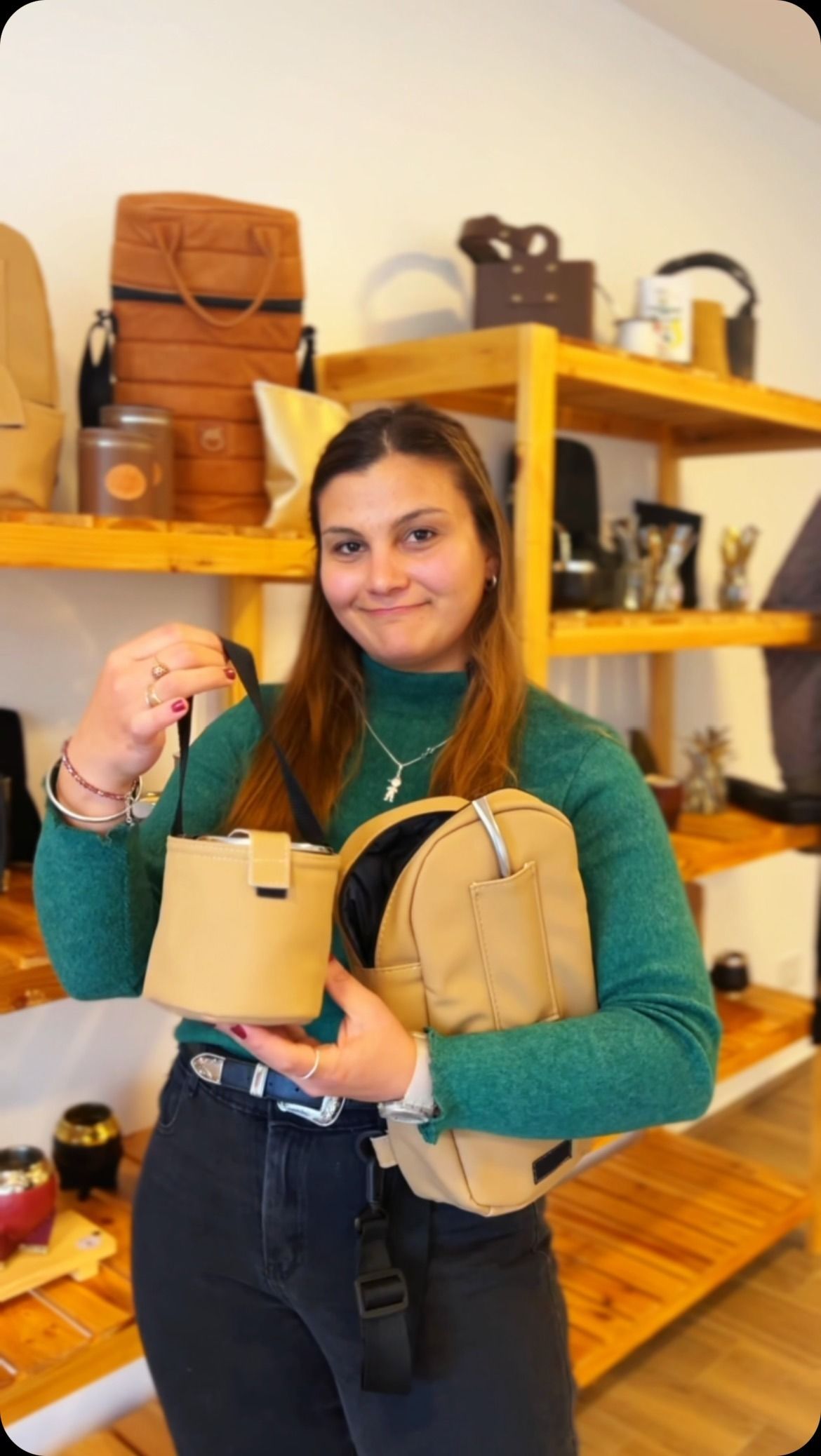 Mujer con bolsas beige en una tienda, con camisa verde y vaqueros. Estante al fondo.