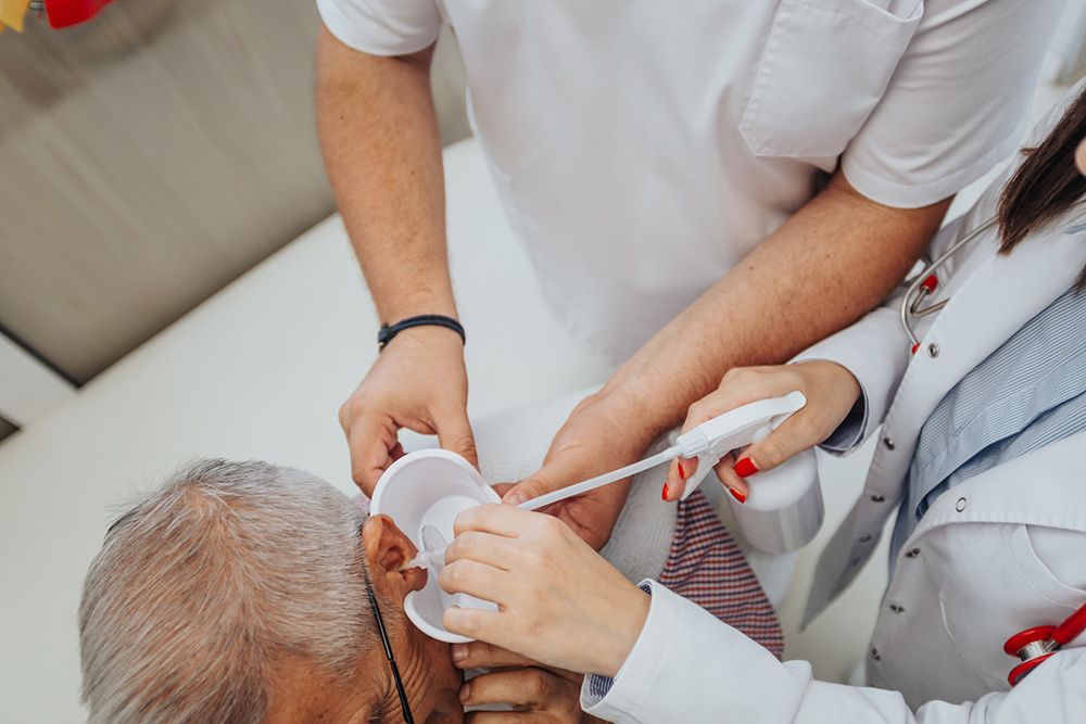 Two Medical Professionals Cleaning an Elderly Person's Ear — Simply Clear Ear Care in Tinonee, NSW 