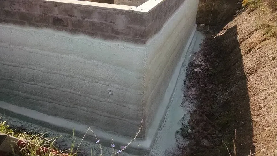 A concrete wall is being waterproofed in a trench.