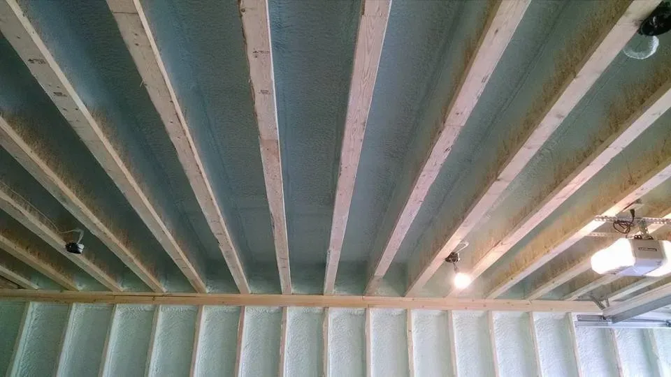 The ceiling of a garage with wooden beams and insulation.