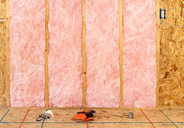 A room with pink insulation on the wall and tools on the floor.