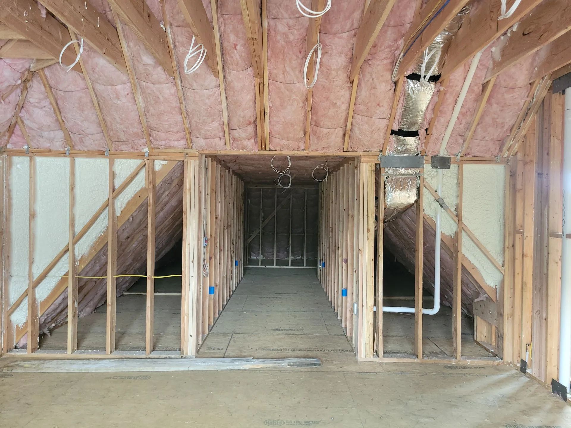 Interior view of a wooden house under construction, with exposed beams, insulation, and wiring.
