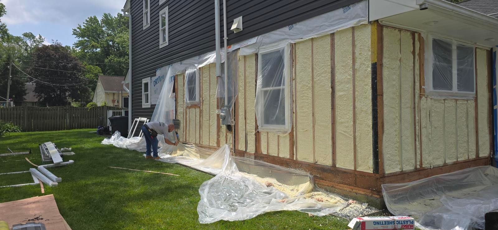A man is spraying foam on the ceiling of an attic.