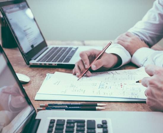 Business man facing a laptop while holding a pen while writing on a paper