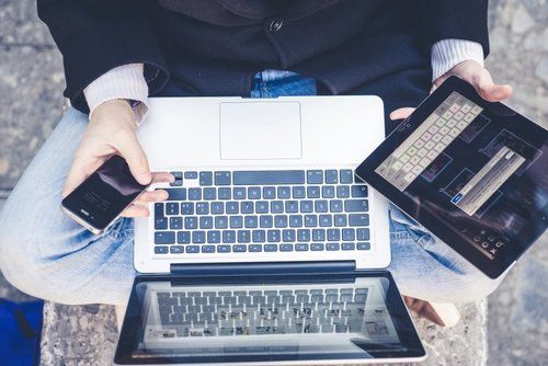 A person is sitting on a bench using a laptop and a tablet.