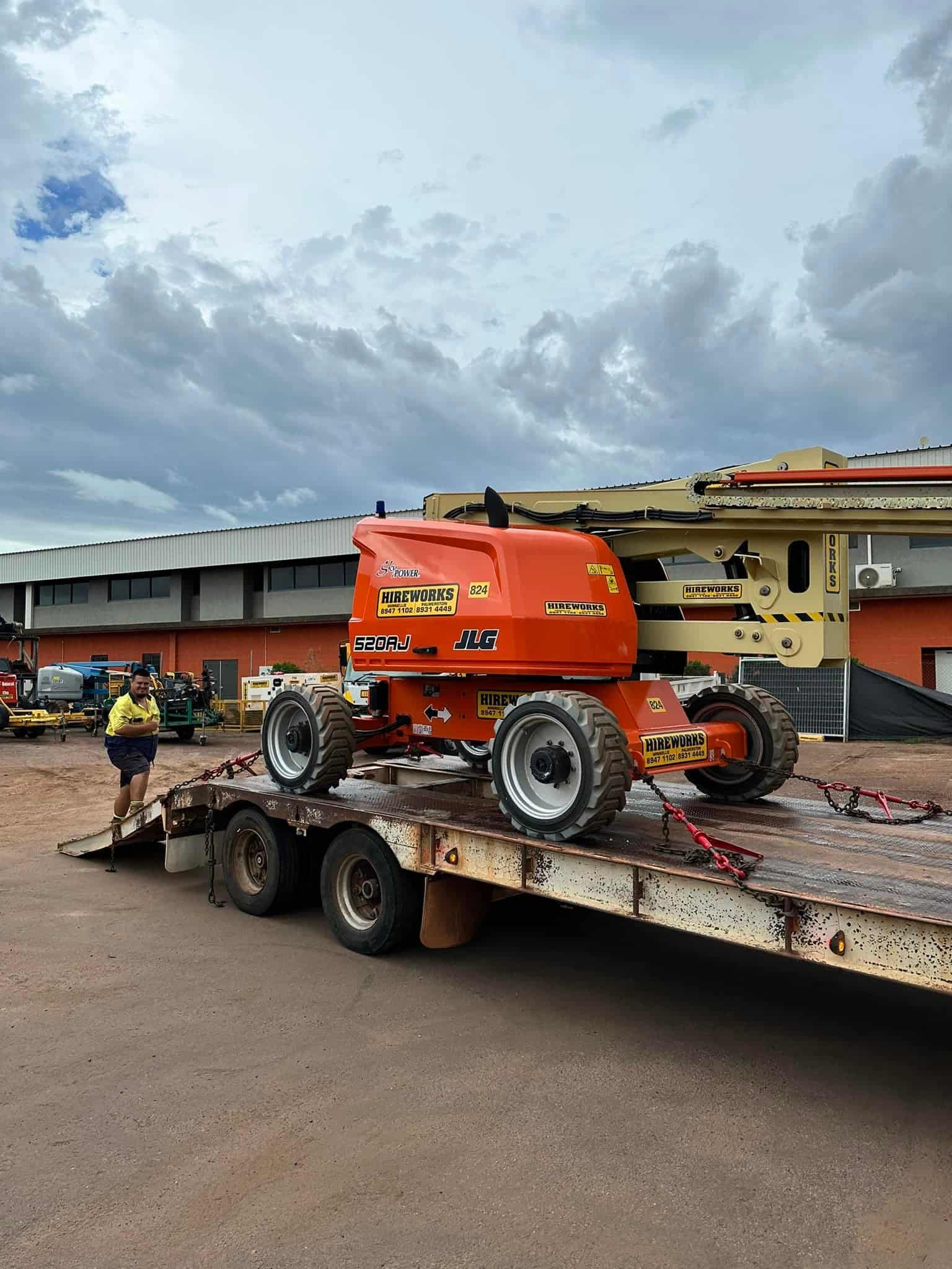 A Man is Standing Next to a Trailer With a Crane on It — Cohen’s Towing & 4WD Recoveries In Alice Springs, NT