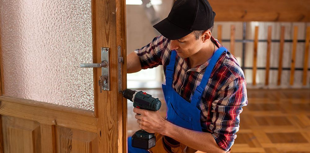 A person in blue overalls drills a door handle on a wooden door.