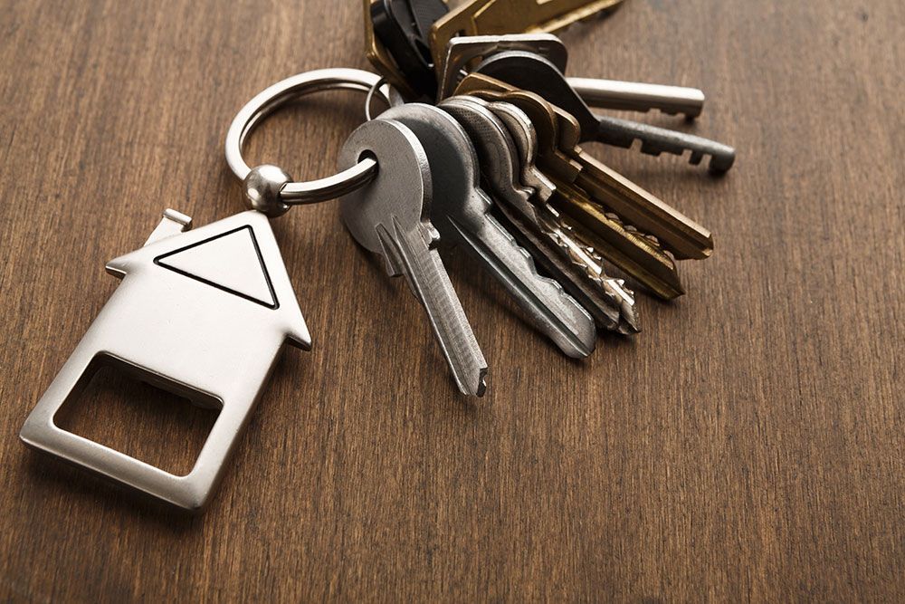 Keys on a ring with a house-shaped keychain, resting on a wooden surface.