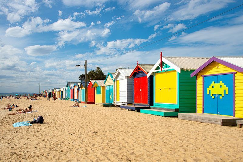 Colorful beach huts lined up on a sandy beach under a blue sky.