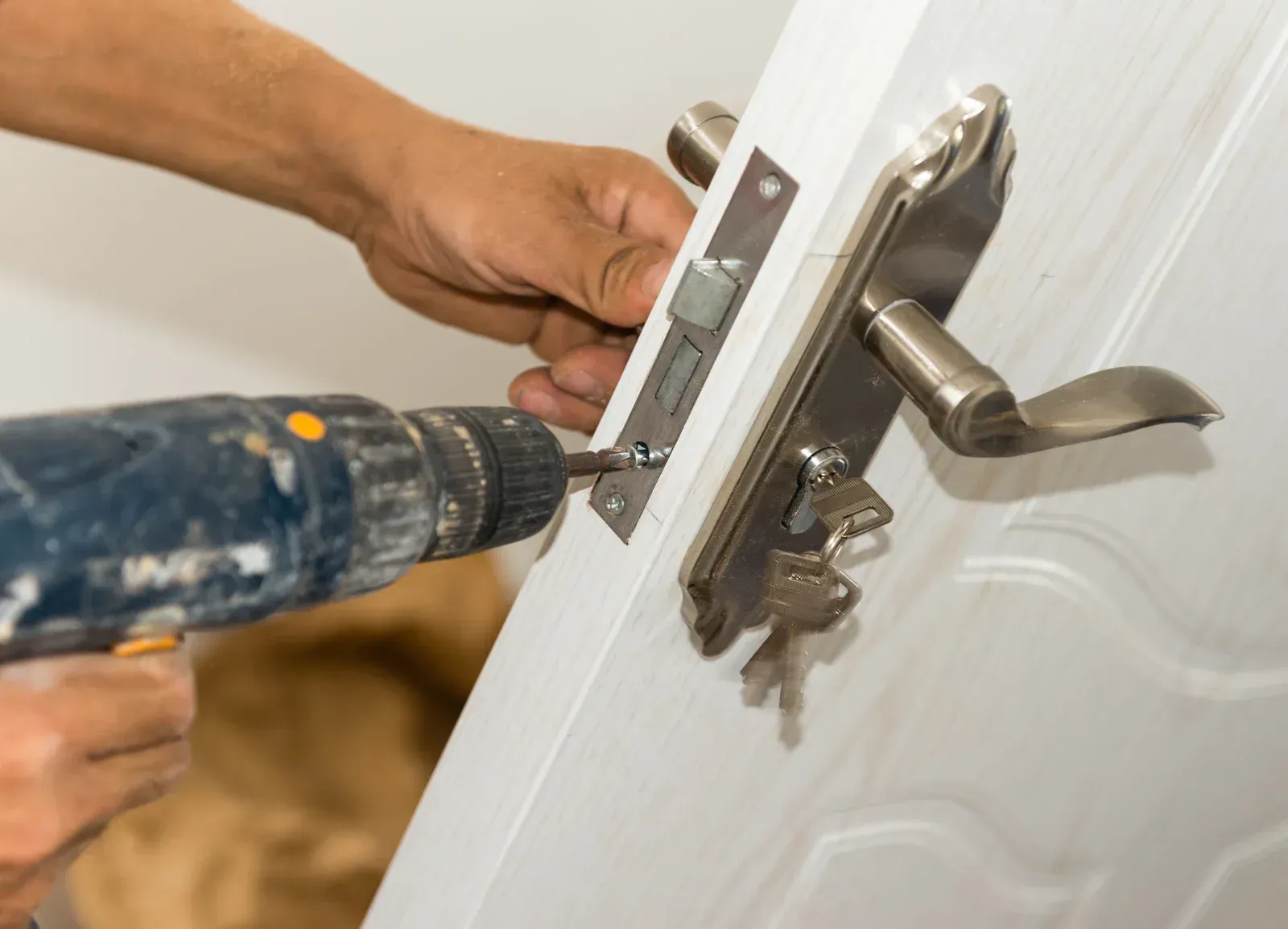 Person using a drill to install a silver door handle on a white door.