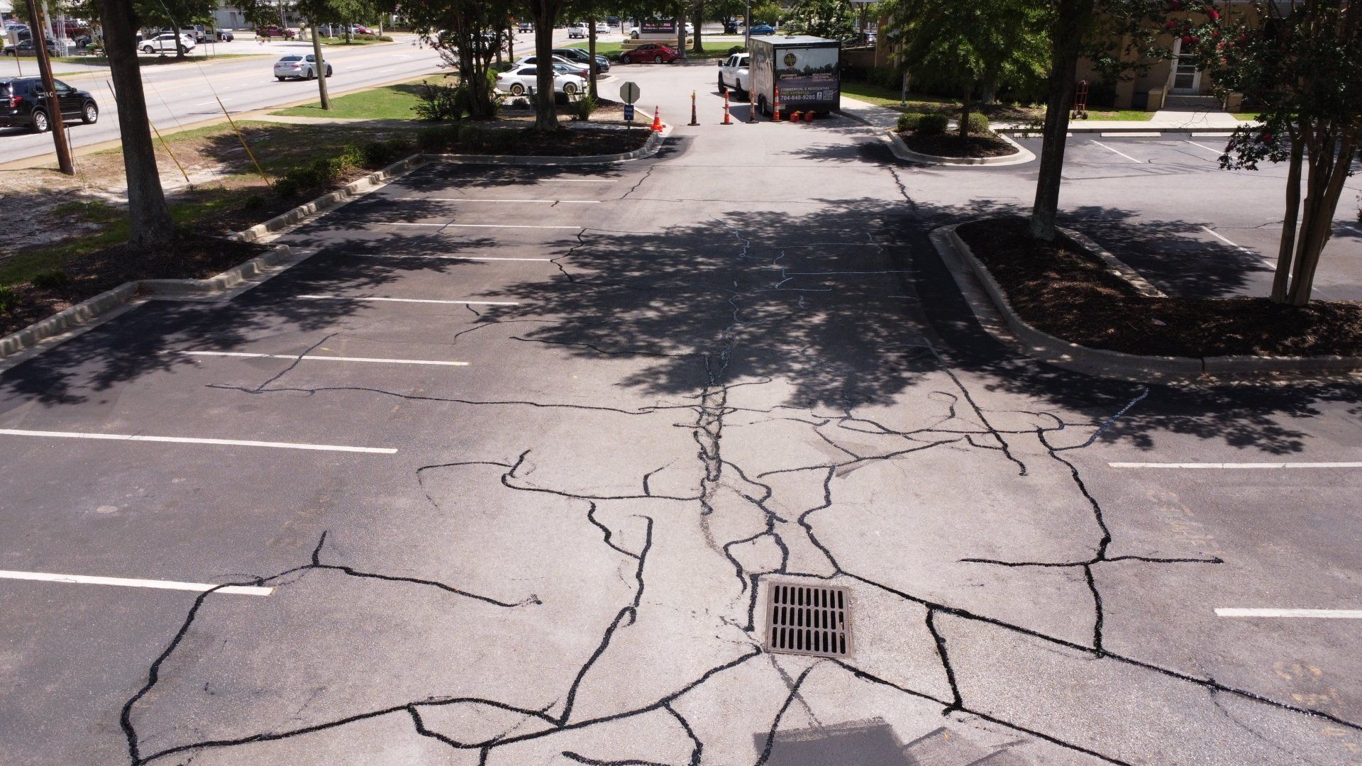 A cracked asphalt road with a drain in the middle