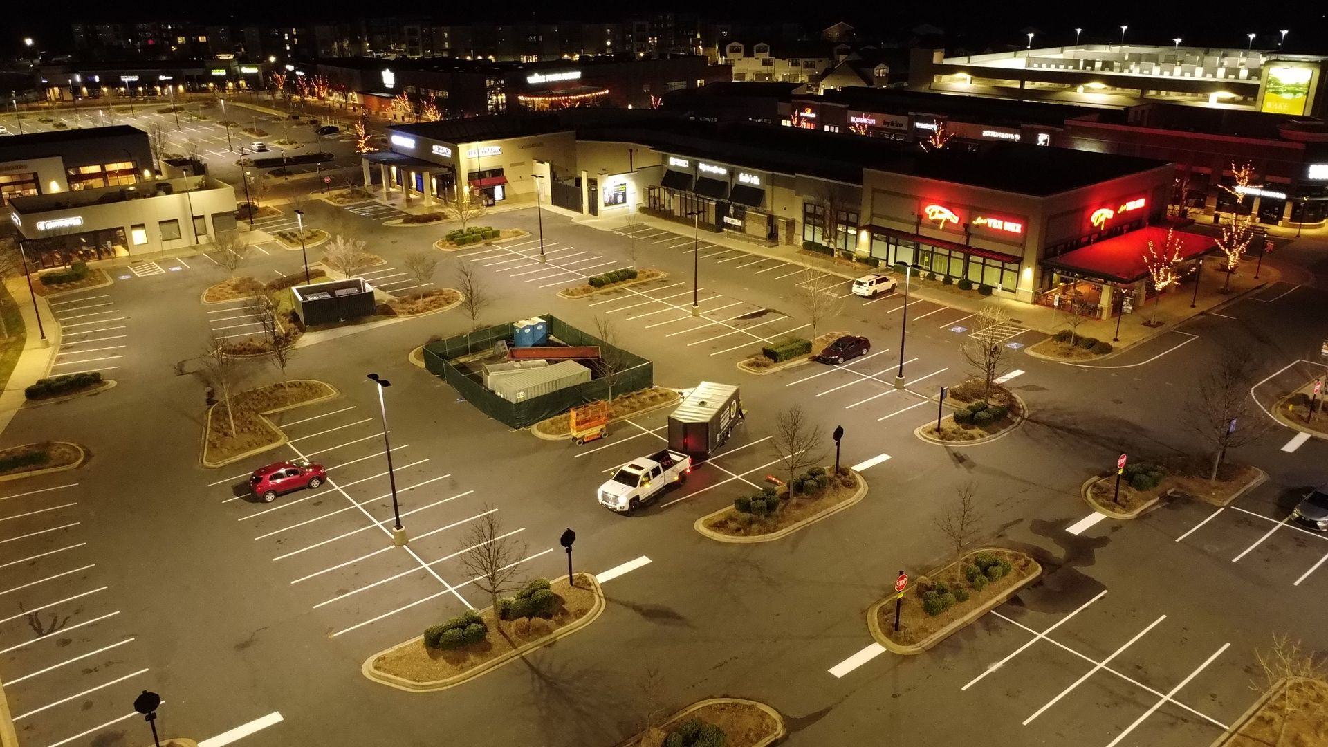 An aerial view of a parking lot at night with cars parked in it.