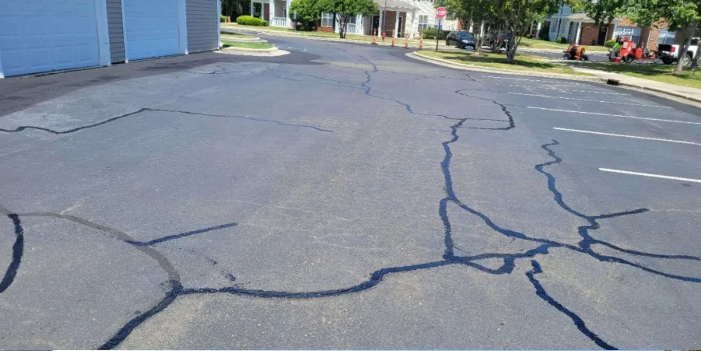 A freshly paved asphalt road at night, with a Lowe's store and parking lot illuminated in the background.