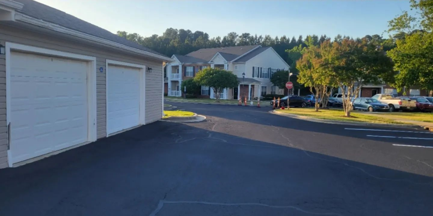 A freshly paved asphalt parking lot lane at night with yellow dashed center lines and overhead lighting.