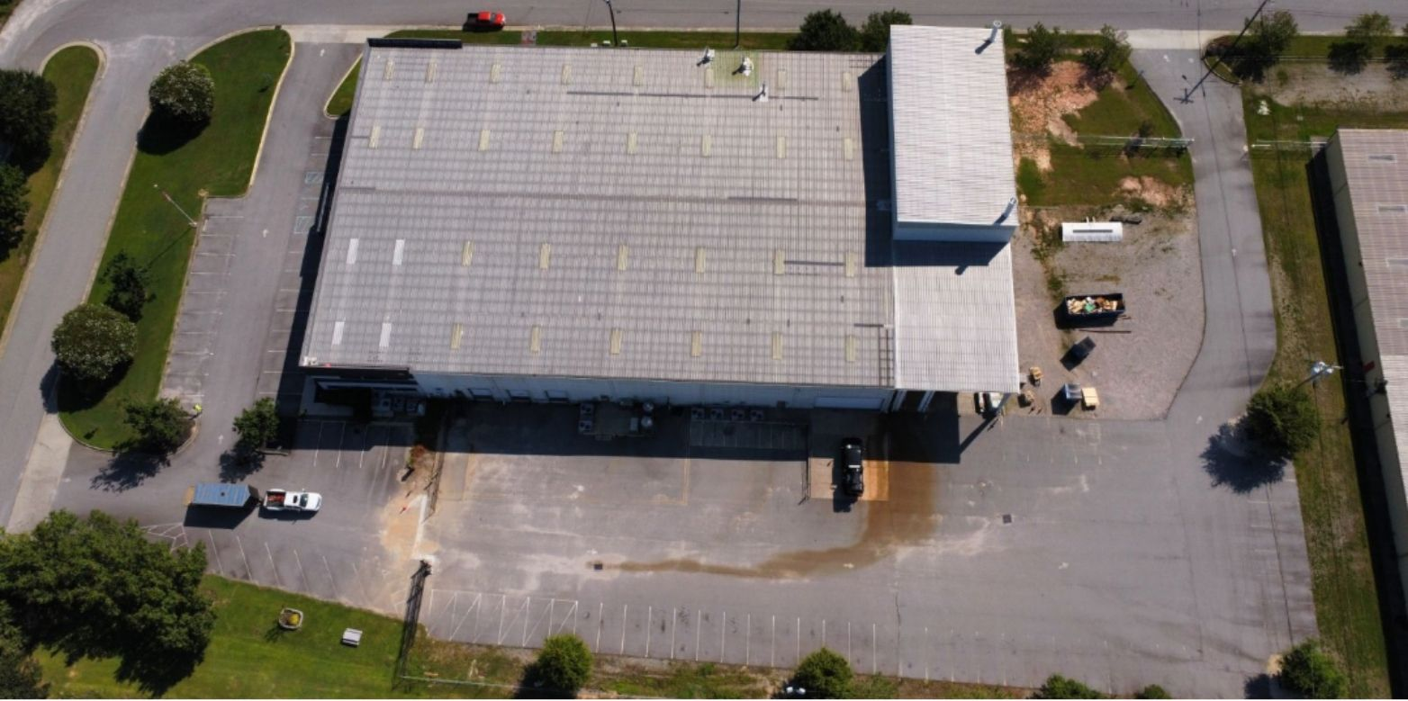 Aerial view of a rectangular warehouse building with a large parking lot and surrounding green space.