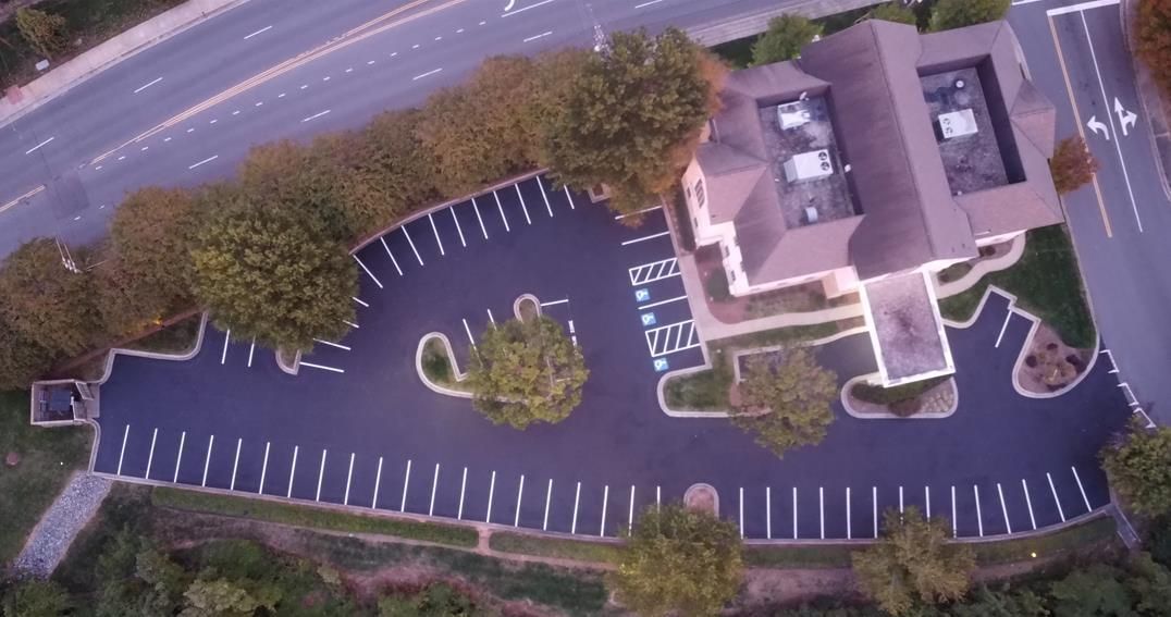 Aerial view of a paved parking lot featuring two accessible parking spaces marked with blue symbols and diagonal stripes.