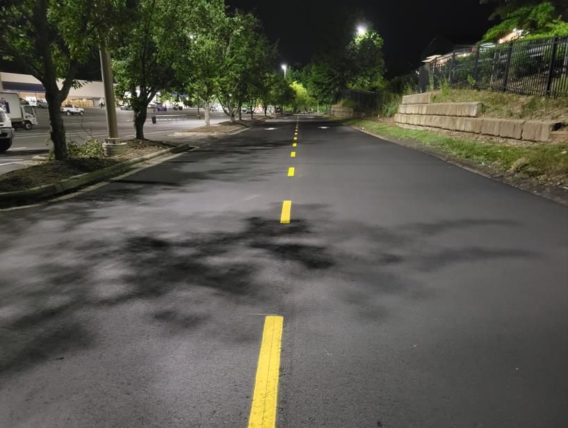 A freshly paved asphalt parking lot lane at night with yellow dashed center lines and overhead lighting.