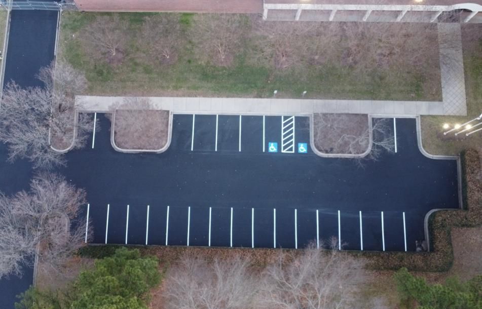 Aerial view of a paved parking lot featuring two accessible parking spaces marked with blue symbols and diagonal stripes.