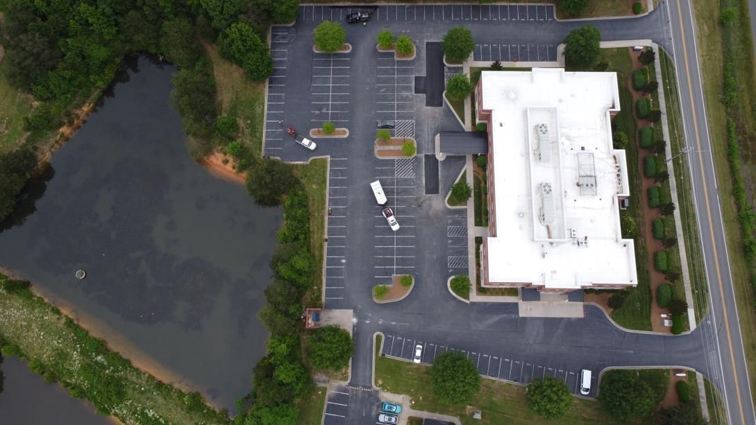 A motorcycle rider practices maneuvering around orange traffic cones in a large, paved parking lot.