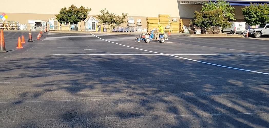 A motorcycle rider practices maneuvering around orange traffic cones in a large, paved parking lot.