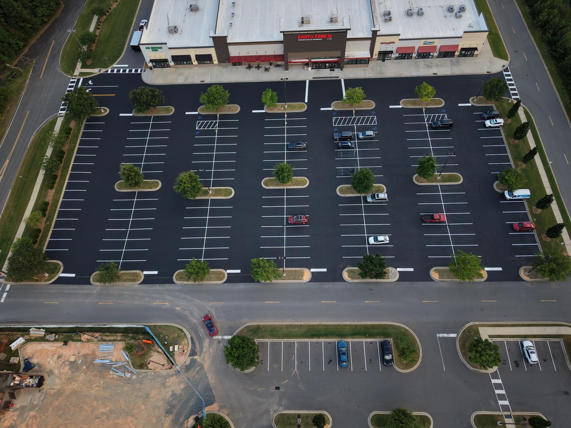 An aerial view of a rectangular warehouse building surrounded by a newly paved asphalt parking lot with white marked spaces.