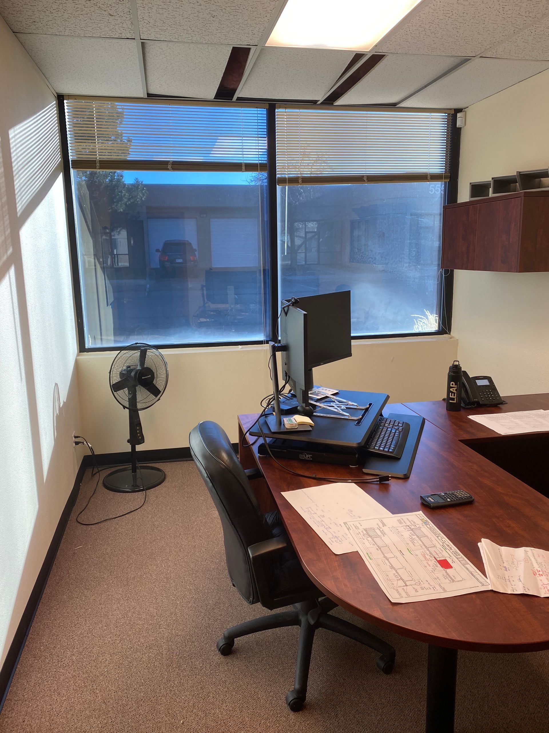 An office with a desk , chair , computer and a fan.