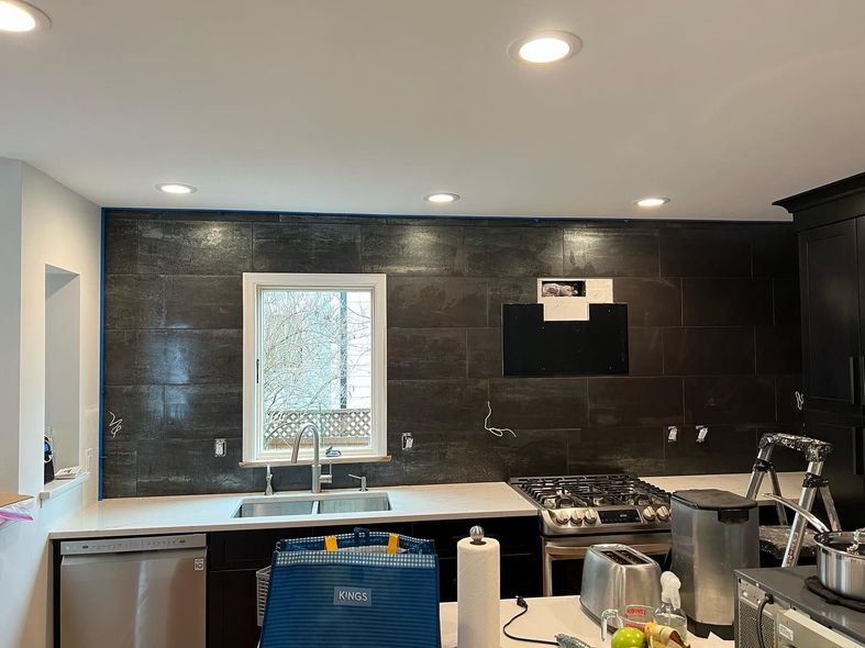 Modern kitchen with dark tile backsplash, white sink, and countertop appliances under recessed ceiling lights