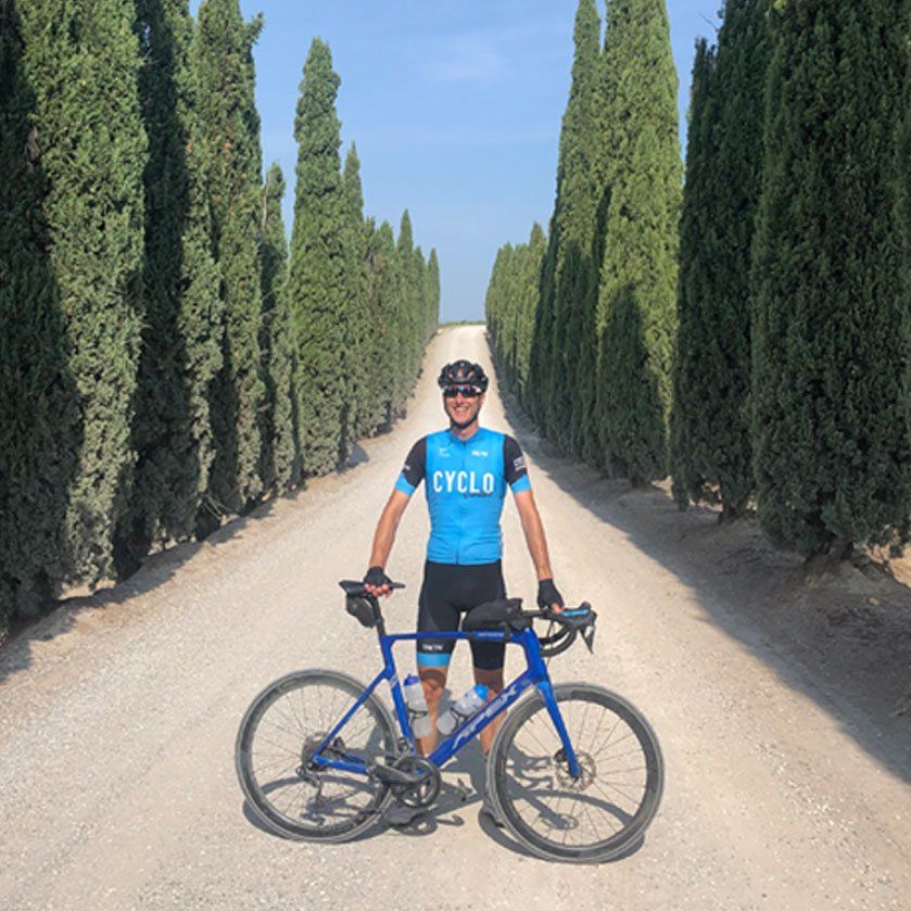 Een man die naast een fiets staat en een blauw shirt draagt ​​met de tekst 'fiets'