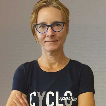 Een vrouw met een bril en een t-shirt met de tekst ‘cycle sportive’ staat met haar armen over elkaar.