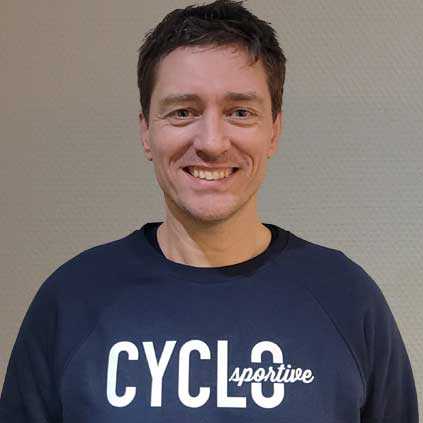 Een man in een blauw sweatshirt met het woord fietsen erop lacht naar de camera.