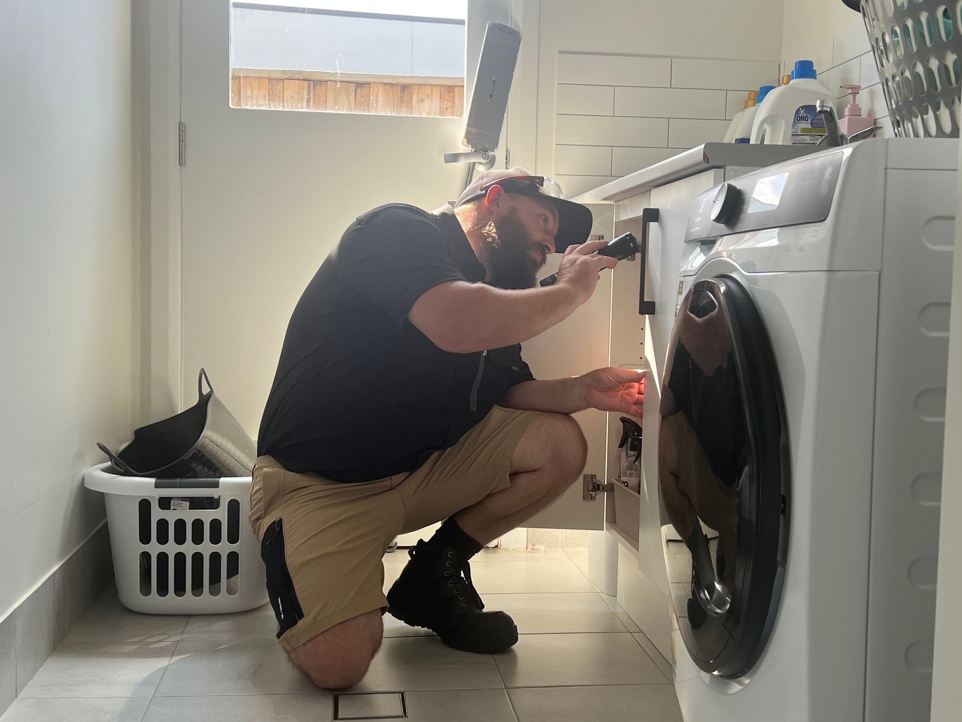 Man Examining a Washing Machine With a Flashlight in a Laundry Room — FUMATEX In Port Macquarie, NSW