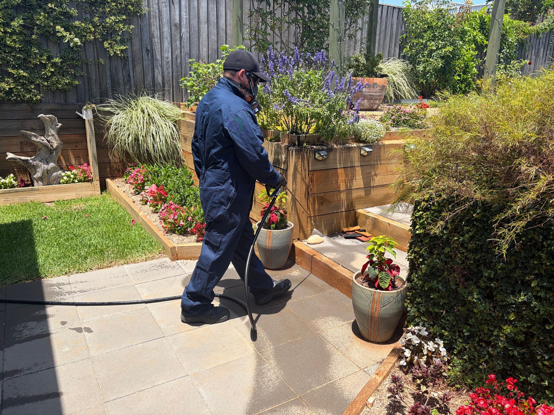 Person in Blue Coveralls Sprays a Backyard Patio With a Hose — FUMATEX In Port Macquarie, NSW