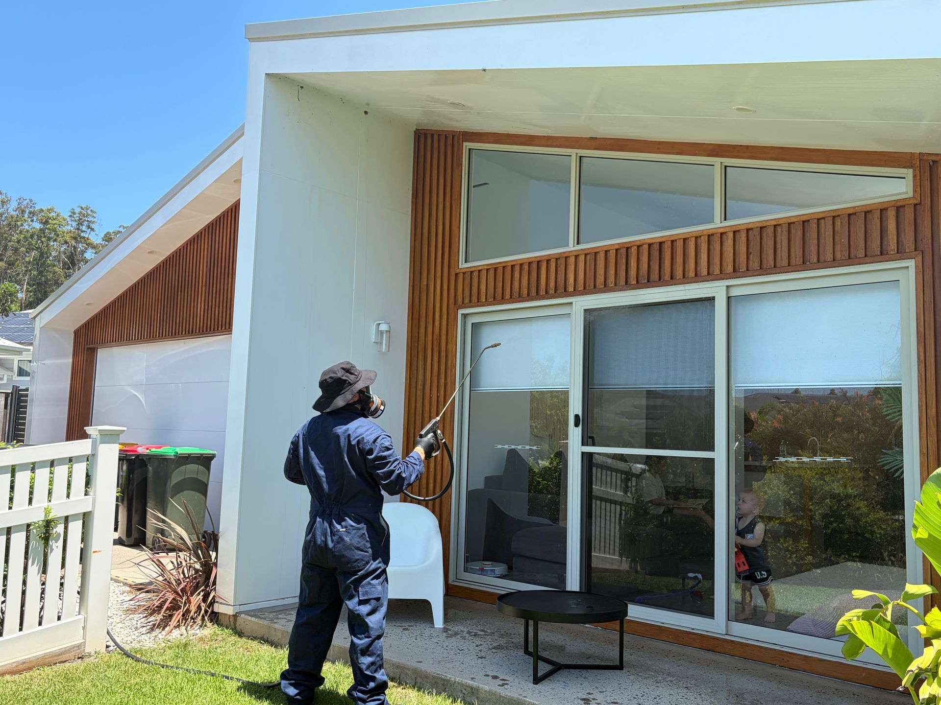 A person in protective gear uses a spray tool at the exterior walls and window area of a modern home  — FUMATEX In Port Macquarie, NSW