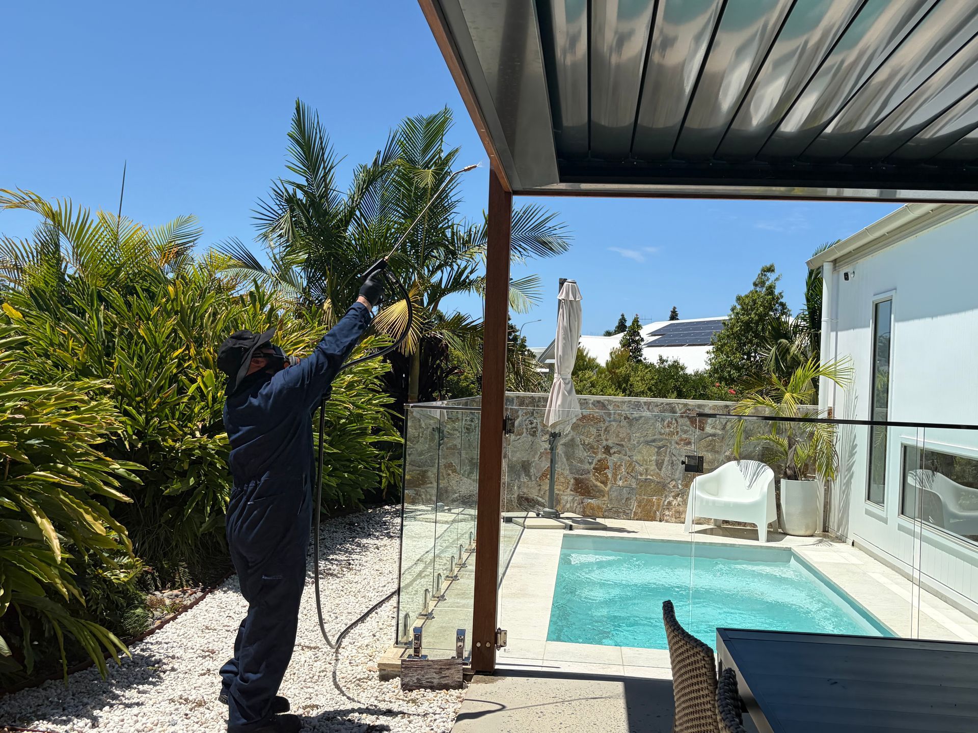 A technician in protective gear sprays a garden near a covered patio and a small backyard swimming pool — FUMATEX In Kempsey, NSW