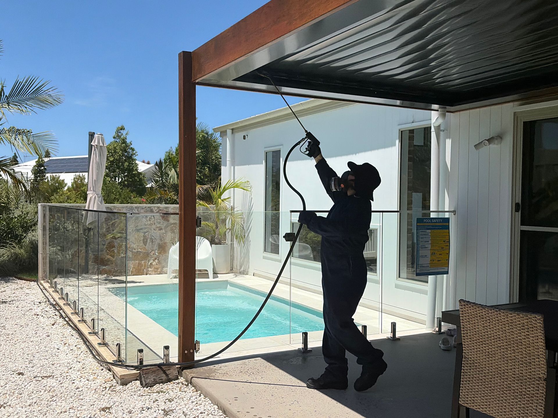 A technician in protective gear sprays a patio roof structure near a backyard swimming pool  — FUMATEX In Laurieton, NSW