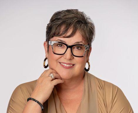 A woman wearing glasses and a necklace is smiling for the camera.