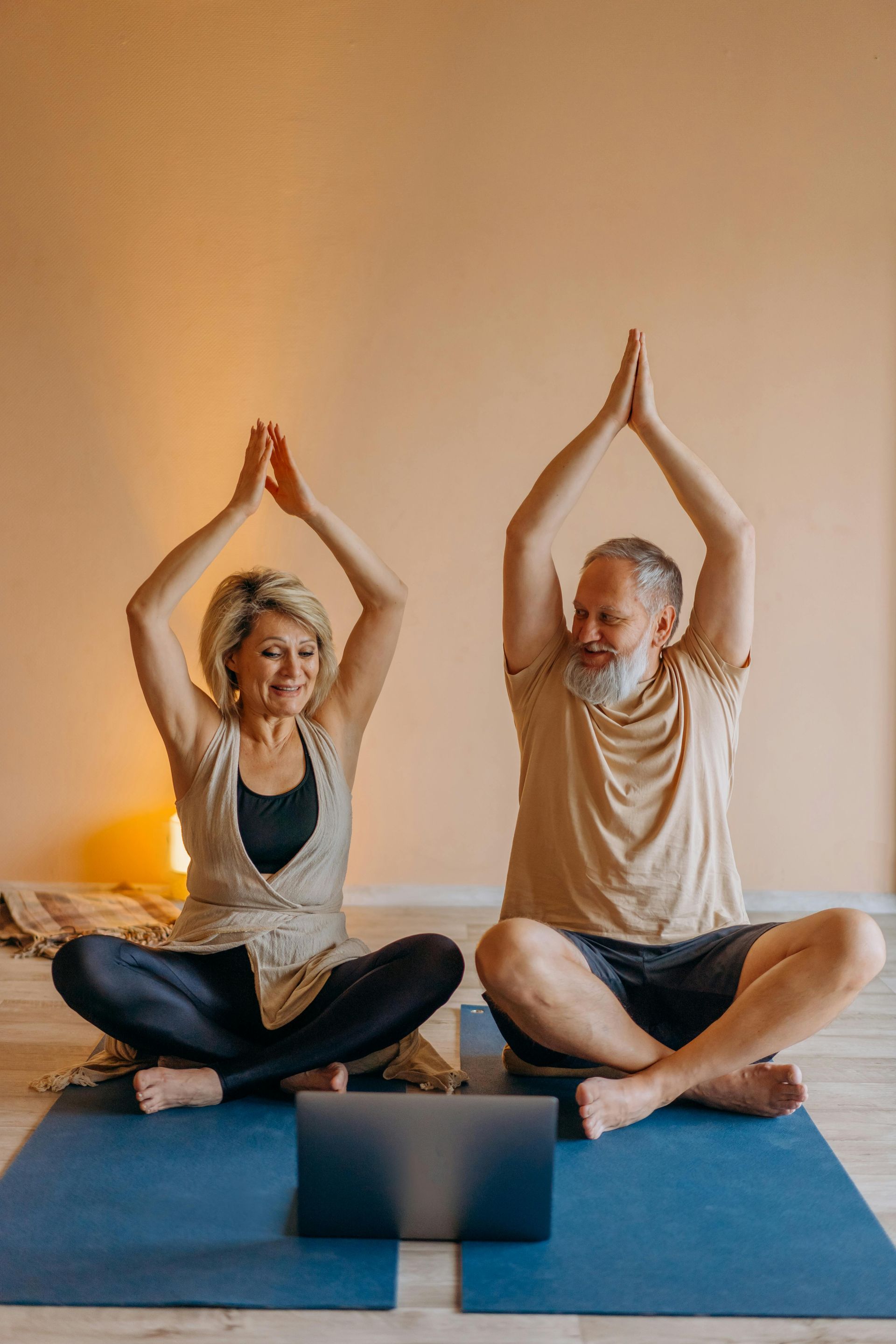 A man and a woman are sitting on yoga mats in front of a laptop.