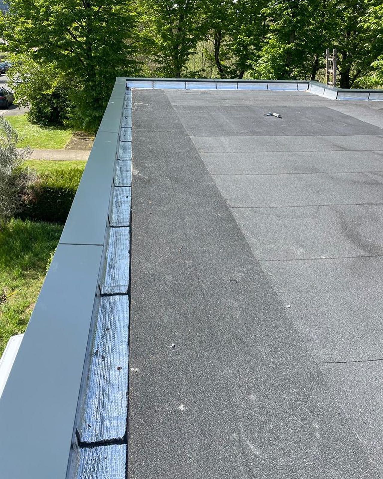 Puits de lumière sur un toit en bardeaux. Des bardeaux gris entourent une fenêtre rectangulaire aux encadrements foncés.