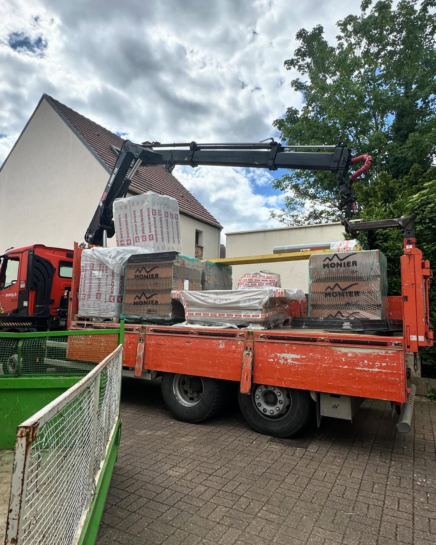 Camion-grue chargé de briques, stationné sur le trottoir près d'une maison, en préparation d'un chantier.