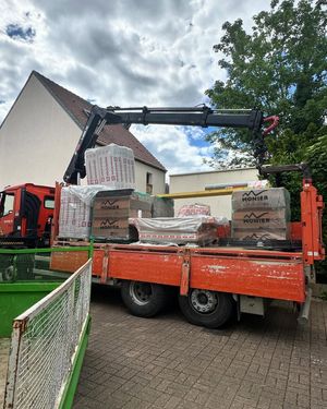 Camion-grue chargé de briques, stationné sur le trottoir près d'une maison, en préparation d'un chantier.