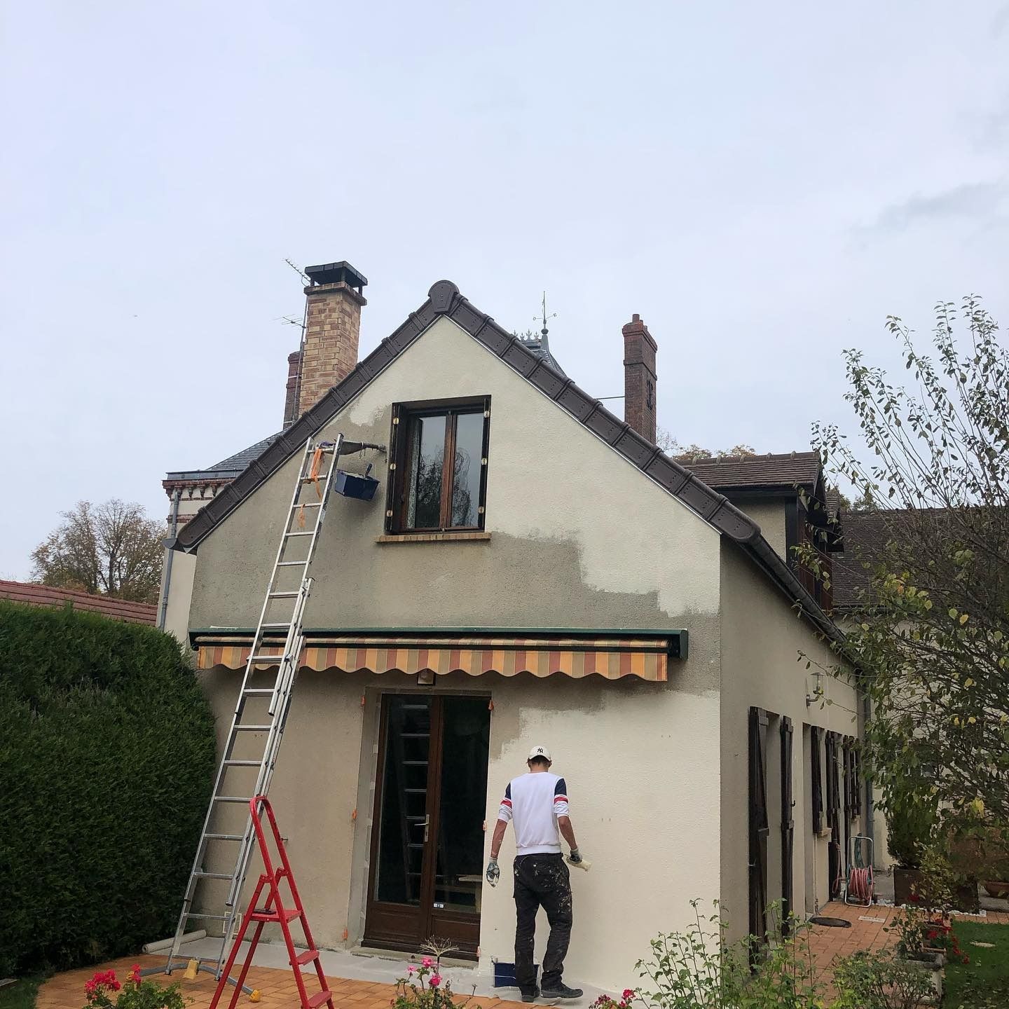 Un couvreur nettoie une lucarne sur un toit de tuiles rouges dans le 78. Une échelle est appuyée contre la maison.
