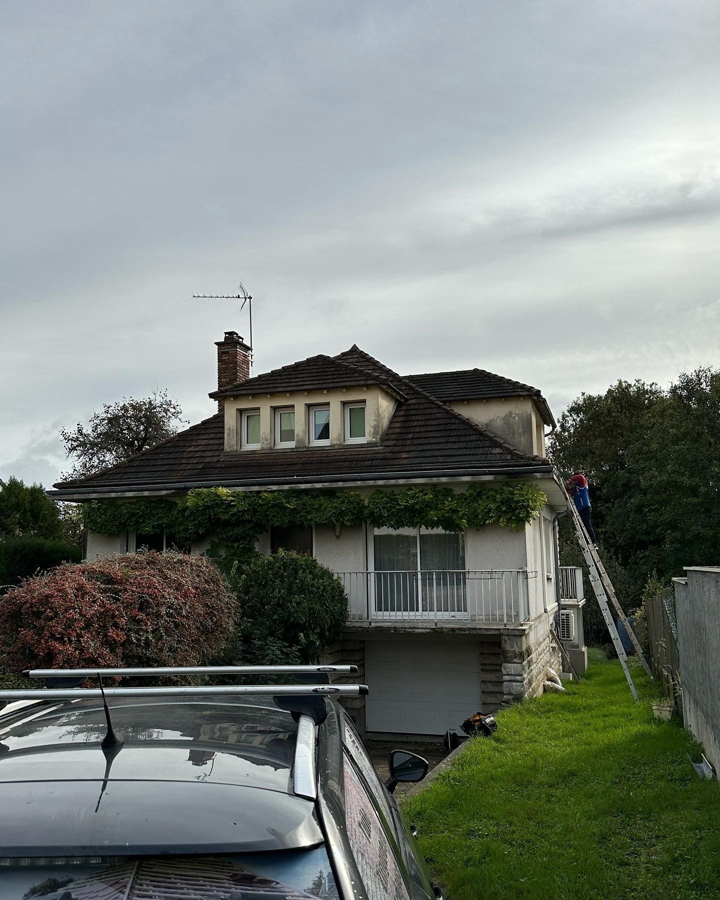 Maison bleue avec des boiseries blanches, des accents de brique et des buissons verts.