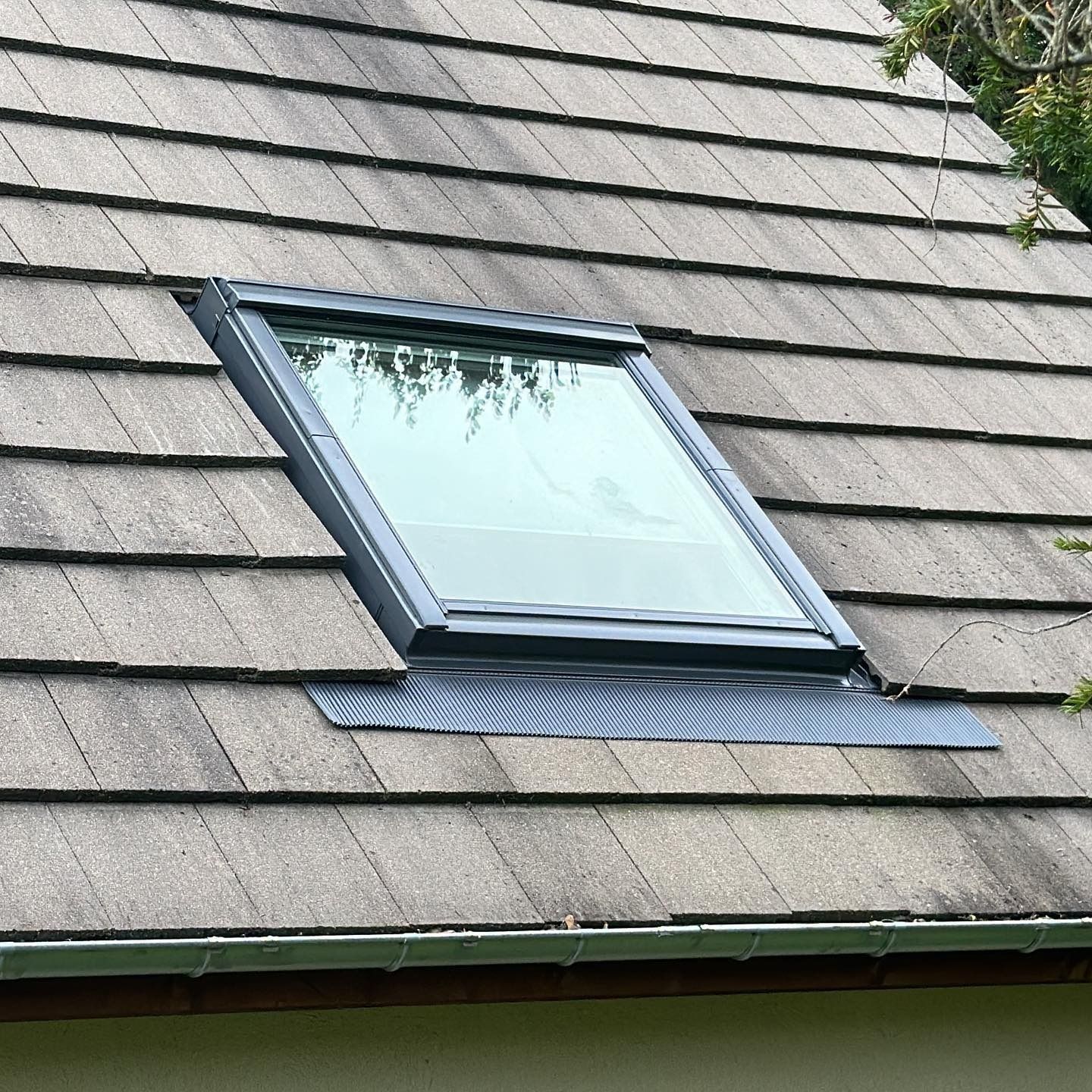 Puits de lumière sur un toit en bardeaux. Le cadre de la fenêtre est sombre et les bardeaux sont abîmés par les intempéries.