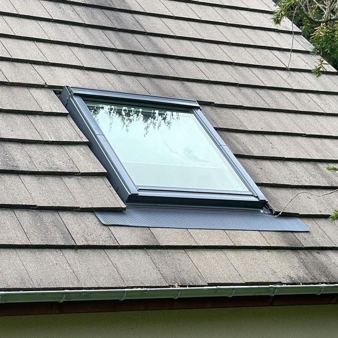 Puits de lumière sur un toit en bardeaux. Le cadre de la fenêtre est sombre et les bardeaux sont abîmés par les intempéries.