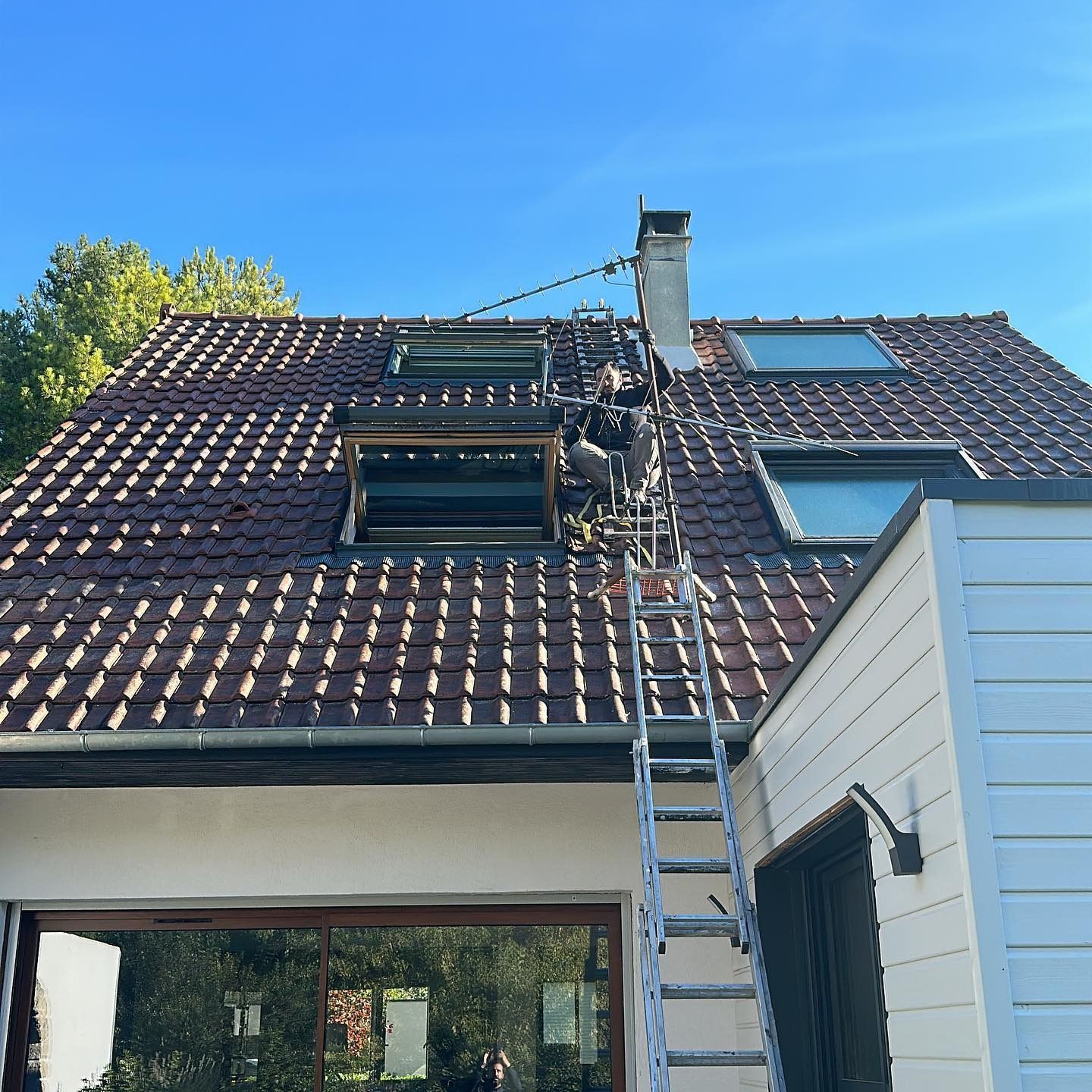 Bâtiment blanc avec une bâche bleue dans le 92, sur une terrasse en bois, une personne sur le toit.