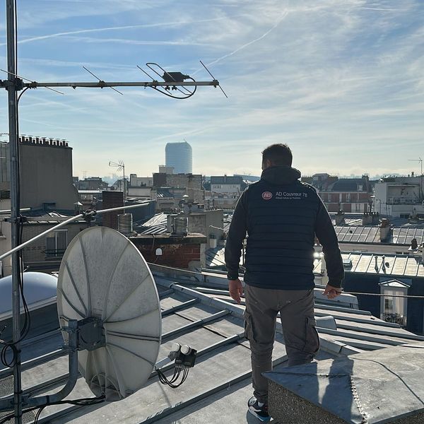 Une personne sur un toit, équipée d'antennes, observe la vue sur la ville par une journée ensoleillée.