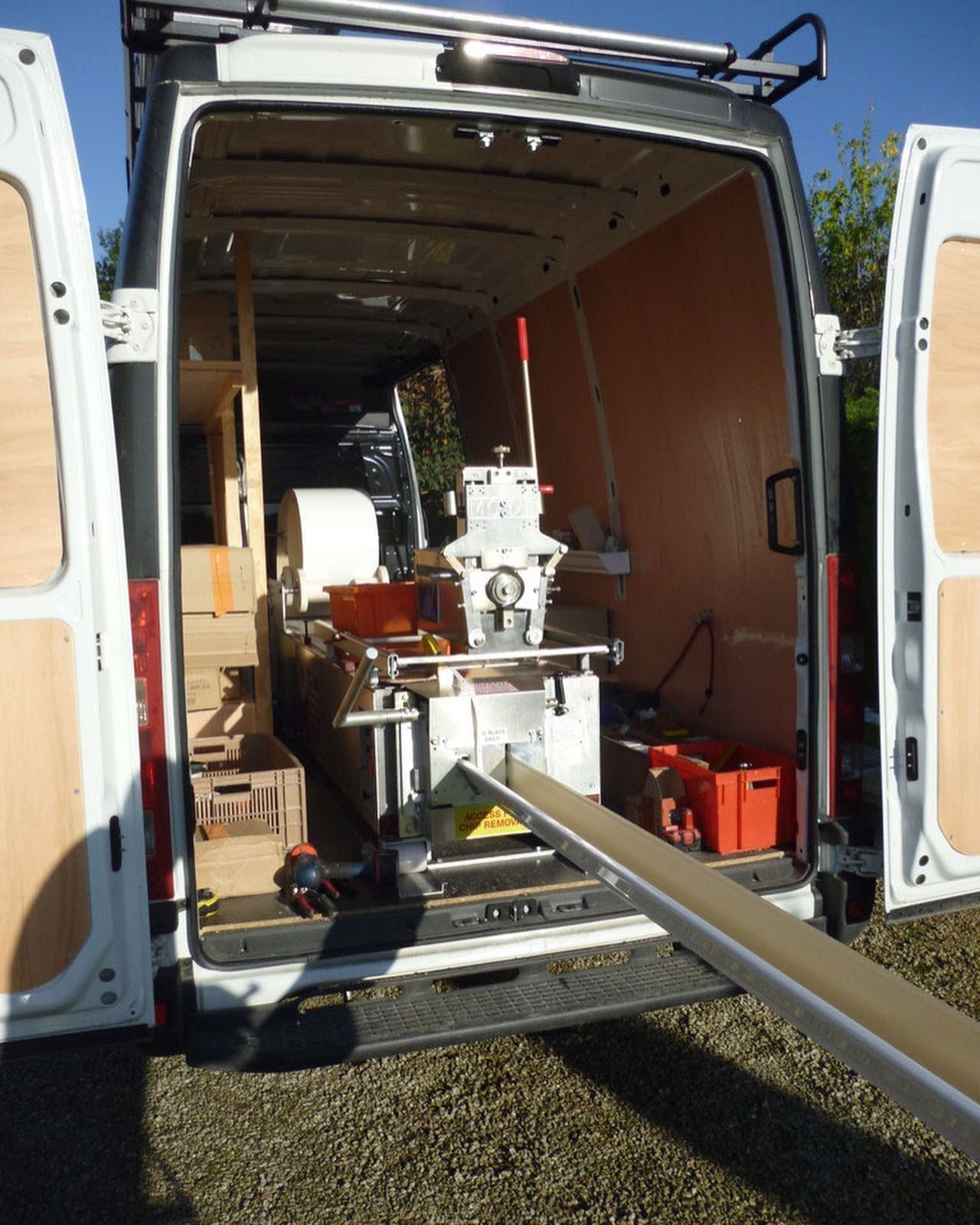 Un homme, perché sur un toit en ardoise, nettoie la gouttière à l'aide d'une longue brosse. Des bâtiments se dressent à l'arrière-plan.